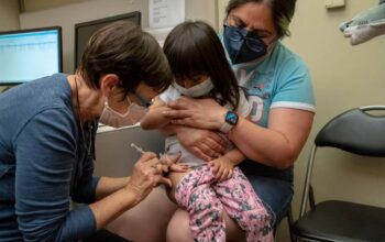 Deni Valenzuela, 2, receives her first dose of the Pfizer Covid-19 vaccination from nurse Deborah Sampson while being held by her mother Xihuitl Mendoza at UW Medical Center